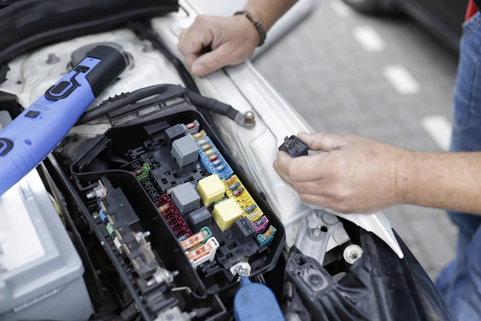 Hands checking relays and fuses in a fuse box